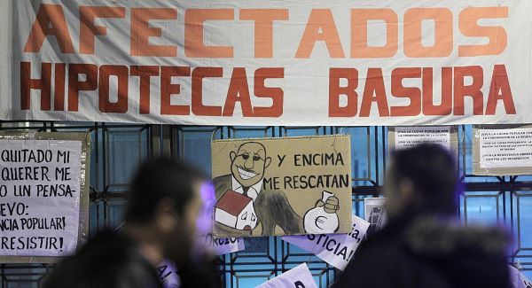 People walk by a banner reading "Rubbish mortgage" and a drawing of a banker reading "They even rescued me" during a protest against evictions outside Bankia's headquarter in Madrid, today. Pic: AP